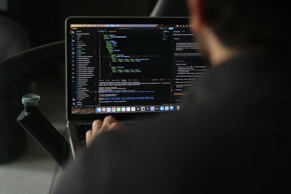 A person working on a laptop inside a vehicle, focusing on a screen displaying lines of code. The laptop has a sleek silver body with a black keyboard, and the screen shows various colored syntax high